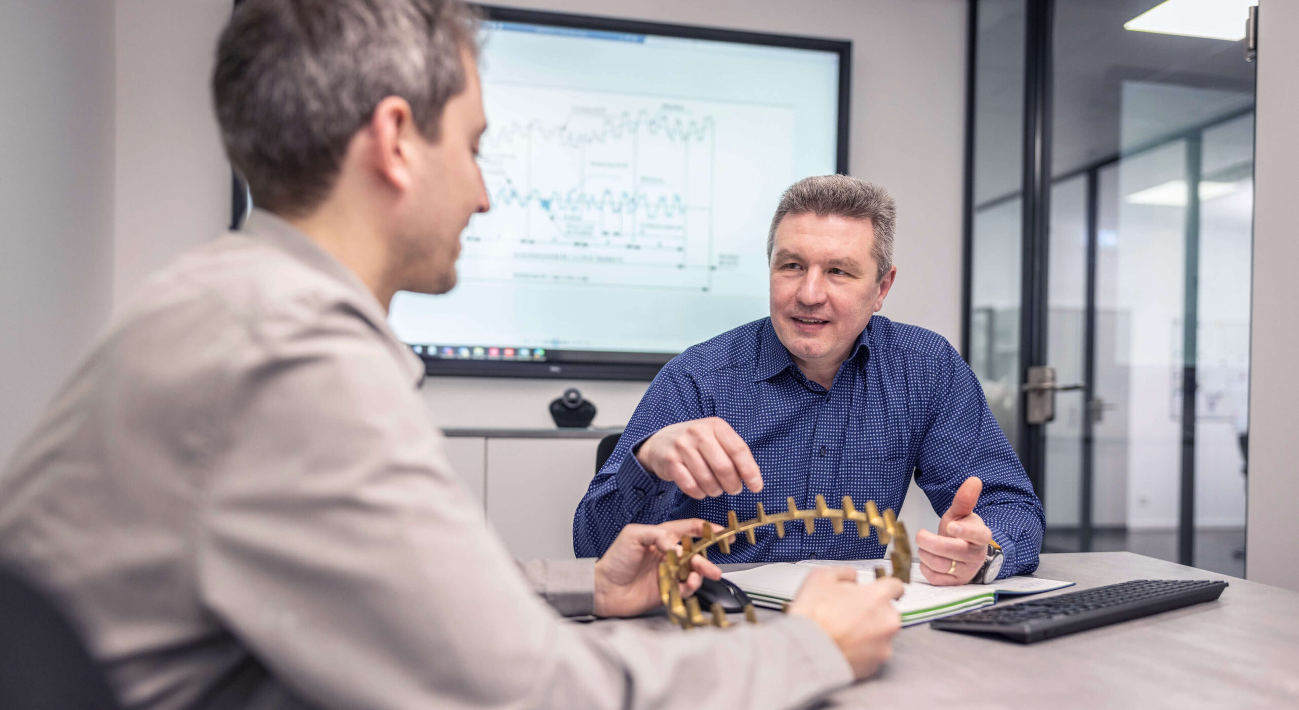 HSP Mitarbeiter im Beratungsgespräch mit einem Kunden, in der Hand einen Wälzlagerkäfig auf Messing